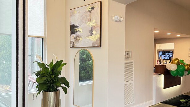 Een modern interieur met een groot raam, een bijzondere plafondlamp, een groot abstract schilderij en een receptiehoek met ballonnen.