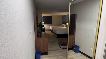Una habitación de hotel con cama, escritorio, silla, espejo y basurero.