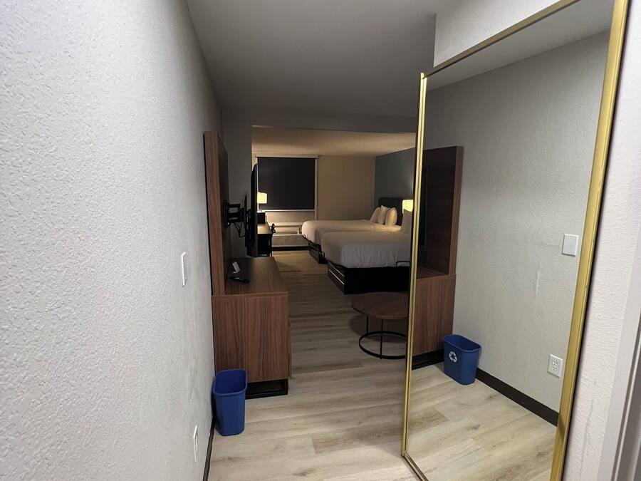 Una habitación de hotel con cama, escritorio, silla, espejo y basurero.