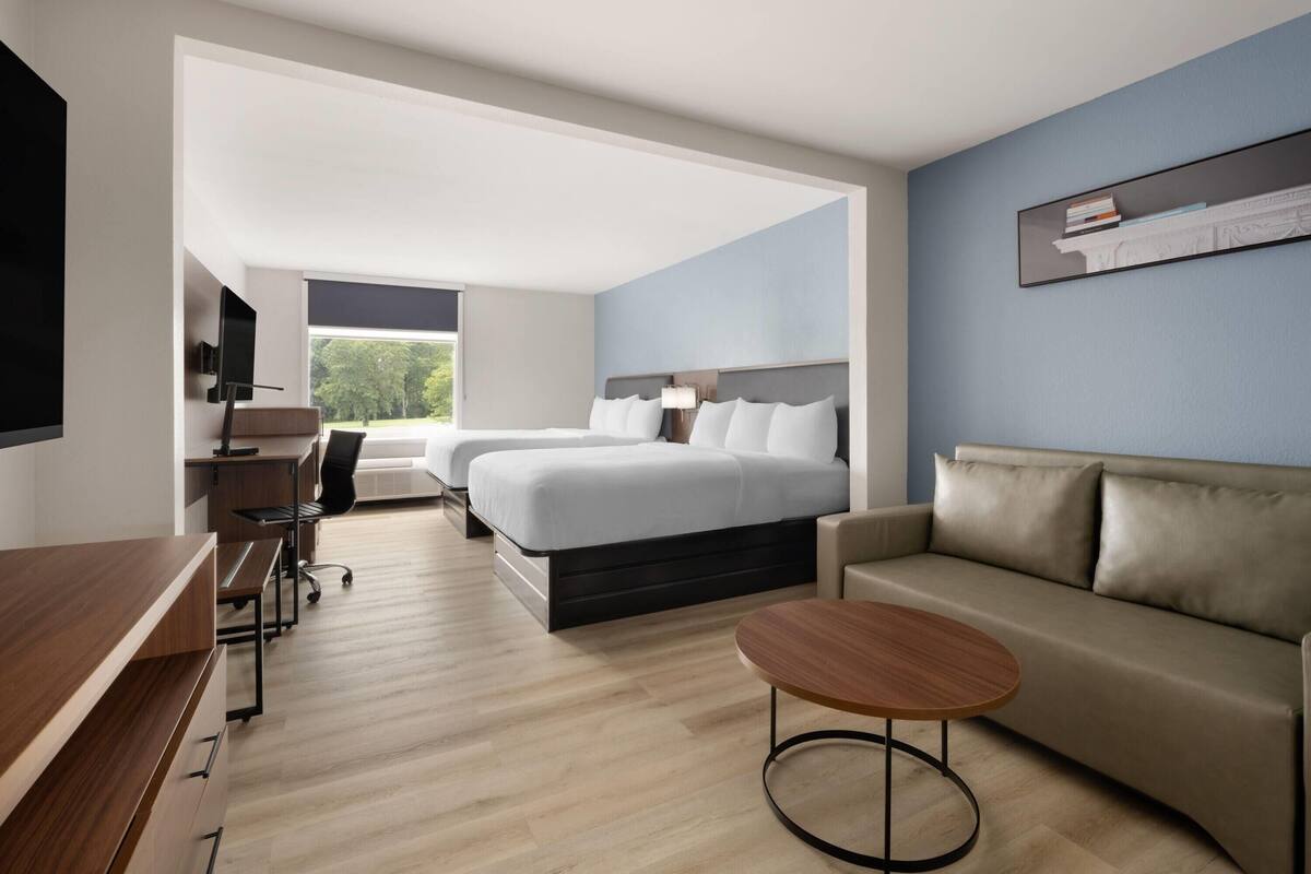 A modern hotel room with a bed, a sofa, a desk, and a TV.