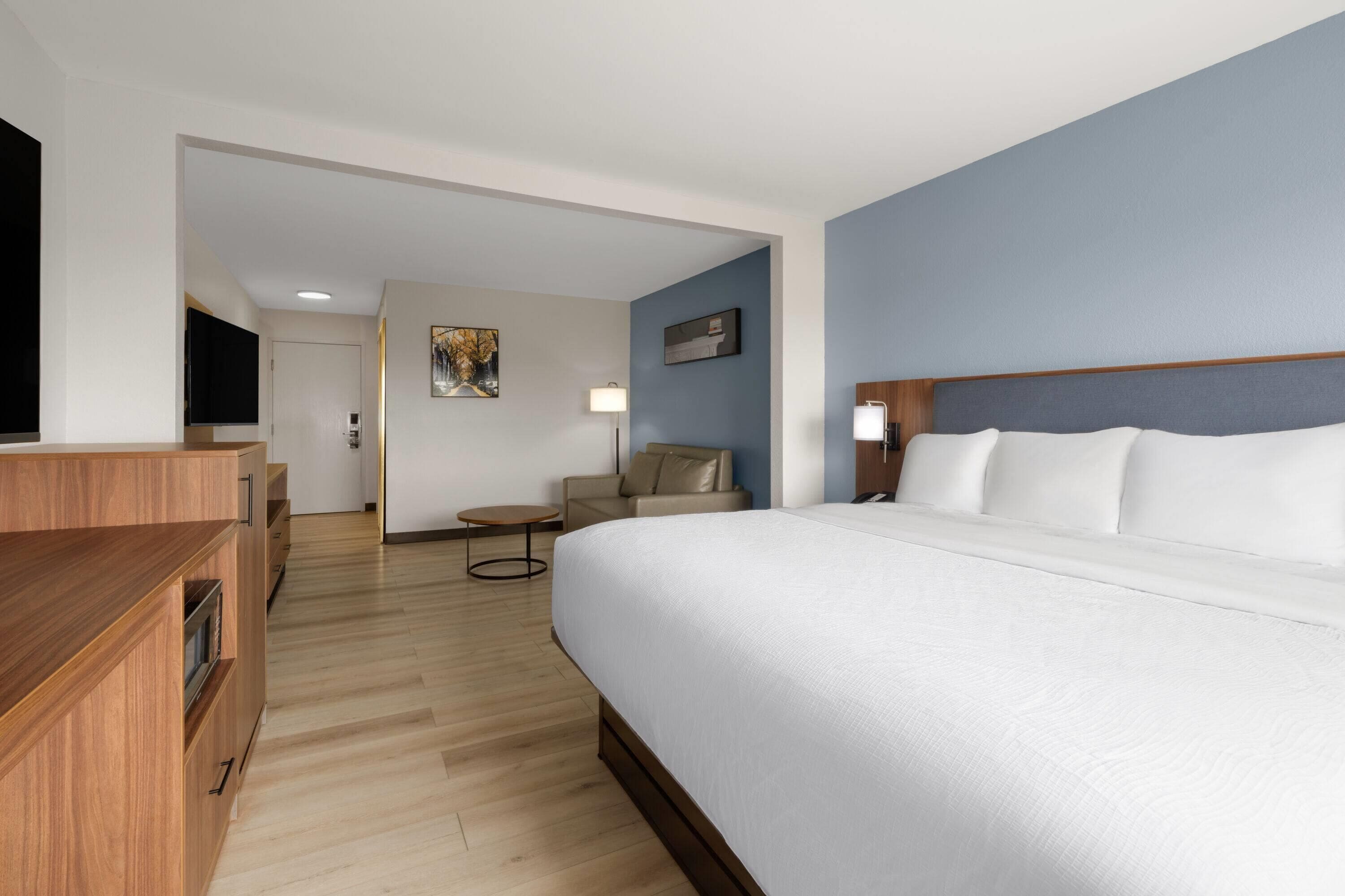 A hotel room with a large bed, a wooden desk, a round table, and a sofa.