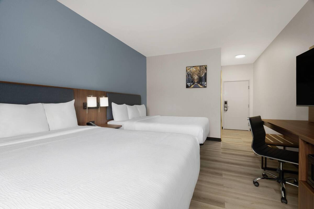A hotel room with two beds, a desk, a chair, and a painting on the wall.