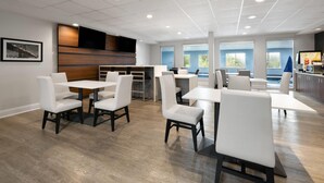 Een ruime eetruimte binnenshuis met meerdere tafels en stoelen, een houten accentmuur en grote ramen die zorgen voor natuurlijk licht.
