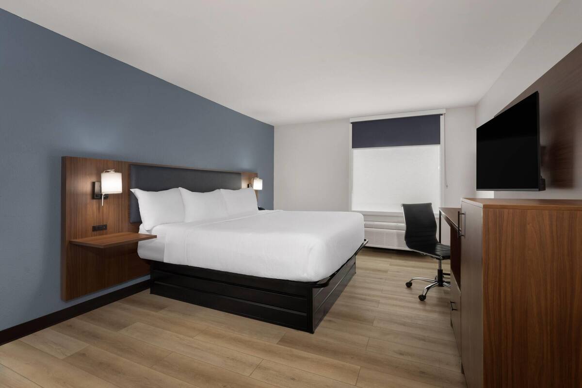 A modern hotel room with a bed, bedside tables, a desk, and a TV.