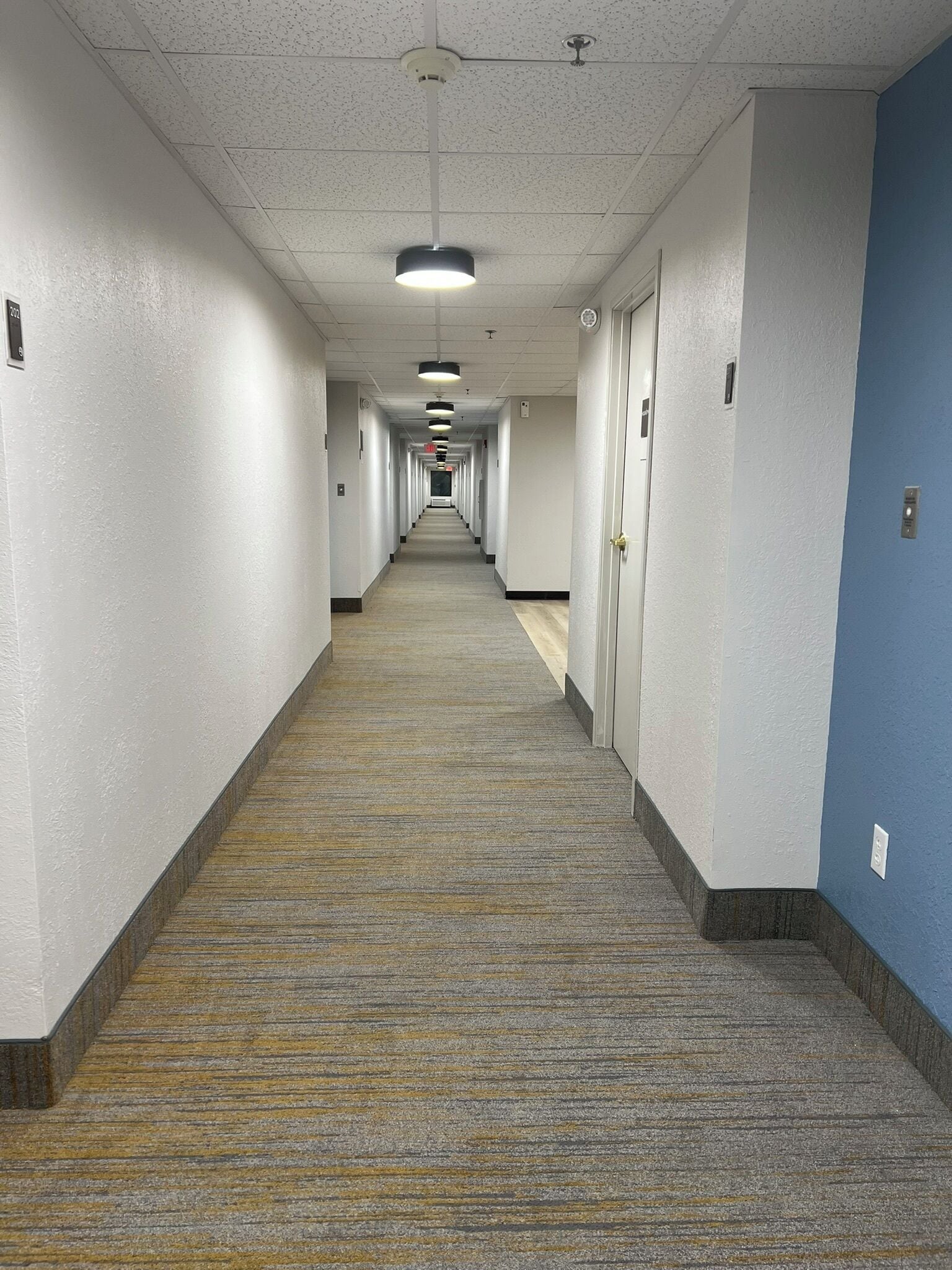 En lång, smal hall med mattbeklädd golv och vita väggar, som leder fram till en dörr i slutet.