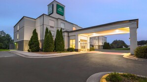 Een modern hotel met een opvallende ingang, een overdekt gebied en een bord waarop staat dat het een Wingate is.