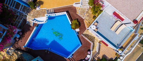 An aerial view of a swimming pool with a wooden deck, surrounded by potted plants and outdoor furniture.