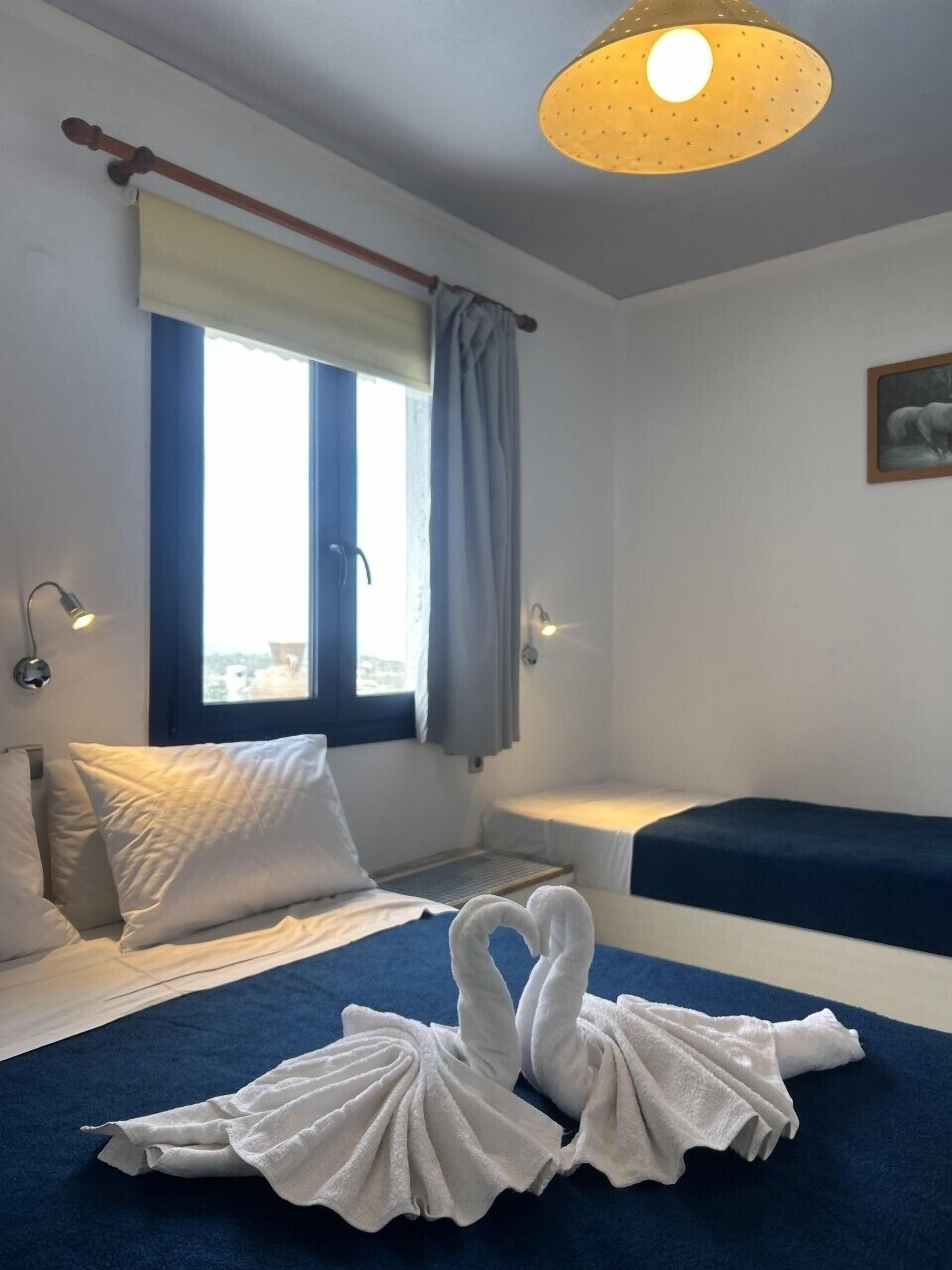 A hotel room with a bed, a window with curtains, a bedside lamp, and a painting on the wall.