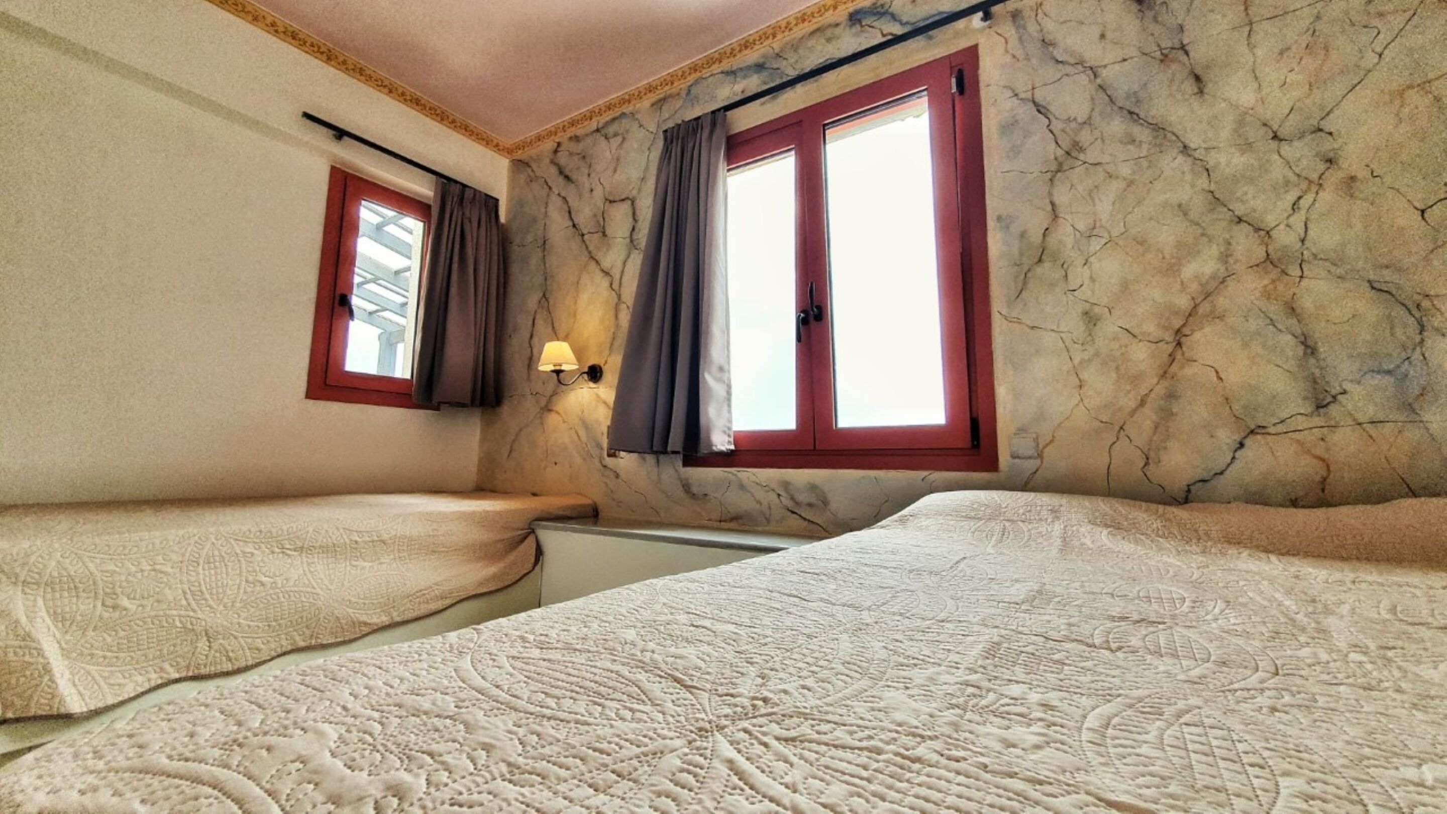Une chambre avec deux lits, une fenêtre avec des rideaux, une lampe et un mur en pierre.