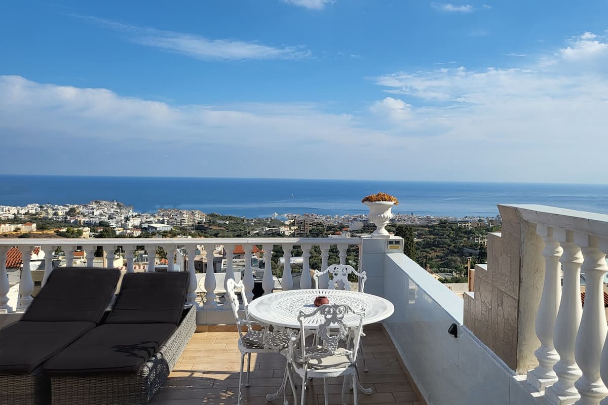 A terrace with a table and chairs, overlooking a coastal cityscape.