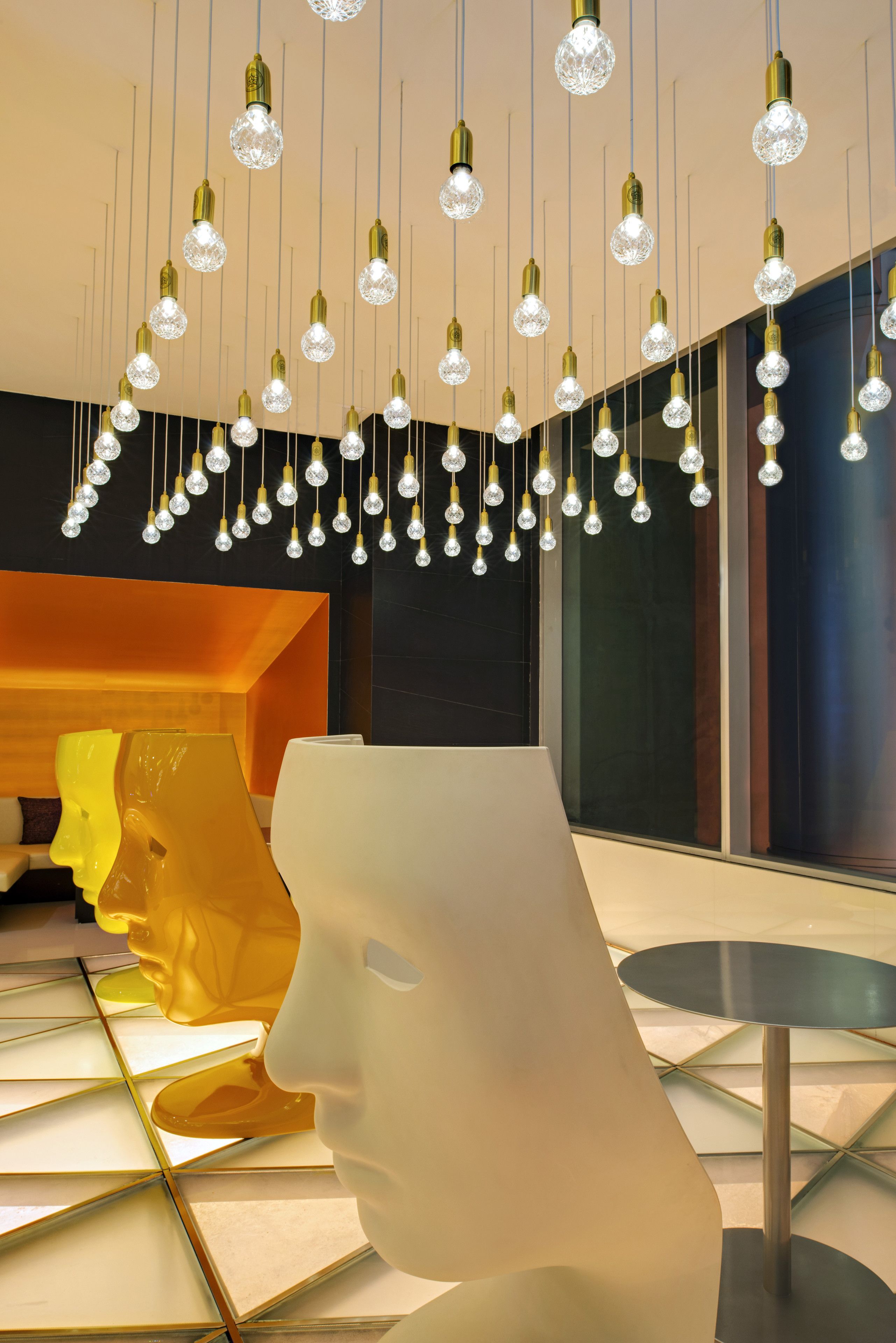 Un intérieur moderne agrémenté de luminaires suspendus, d’un fauteuil blanc aux lignes sculpturales et d’une sculpture abstraite jaune.