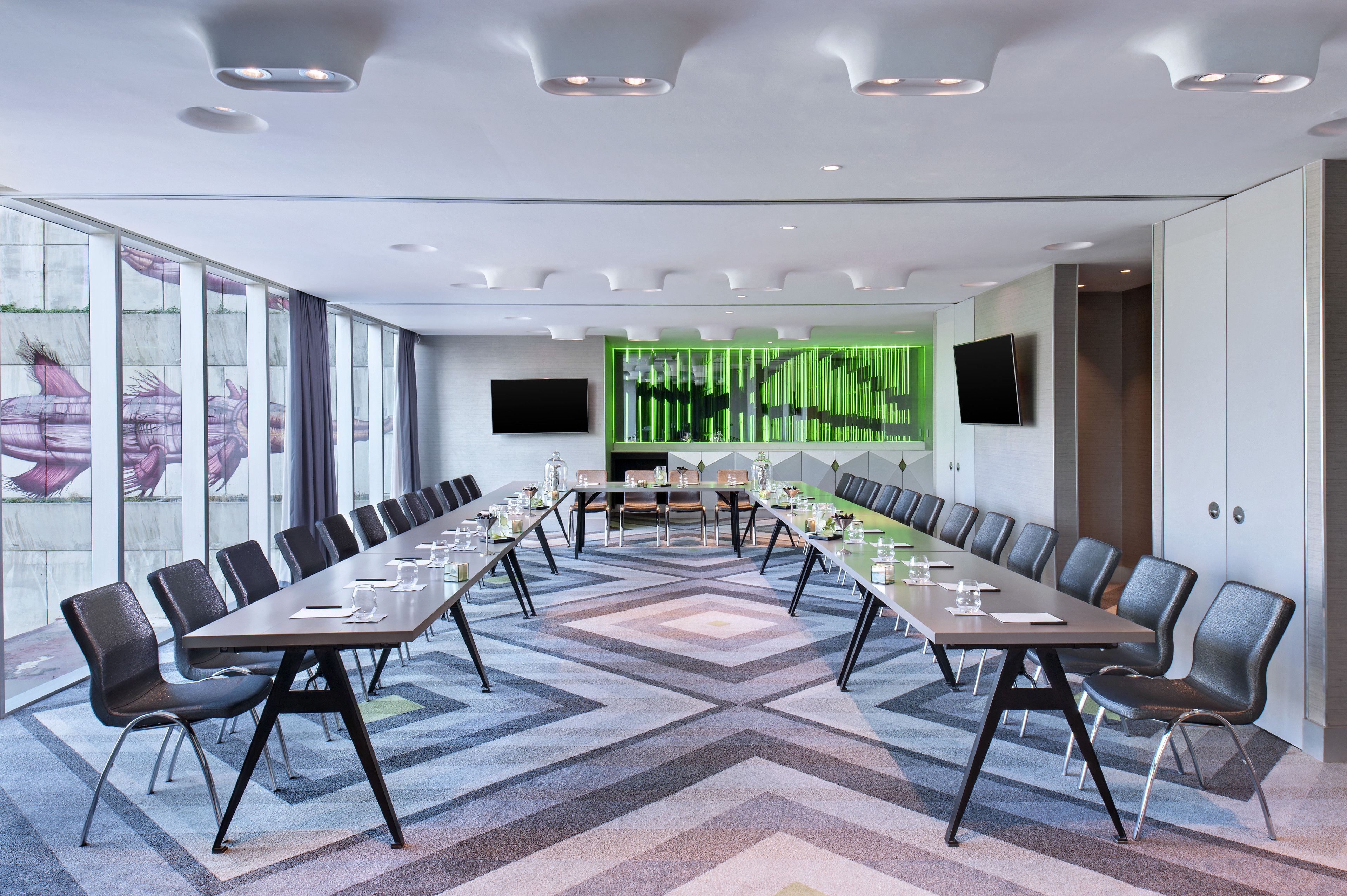 Une salle de conférence avec une longue table, des chaises et un mur décoratif vert.