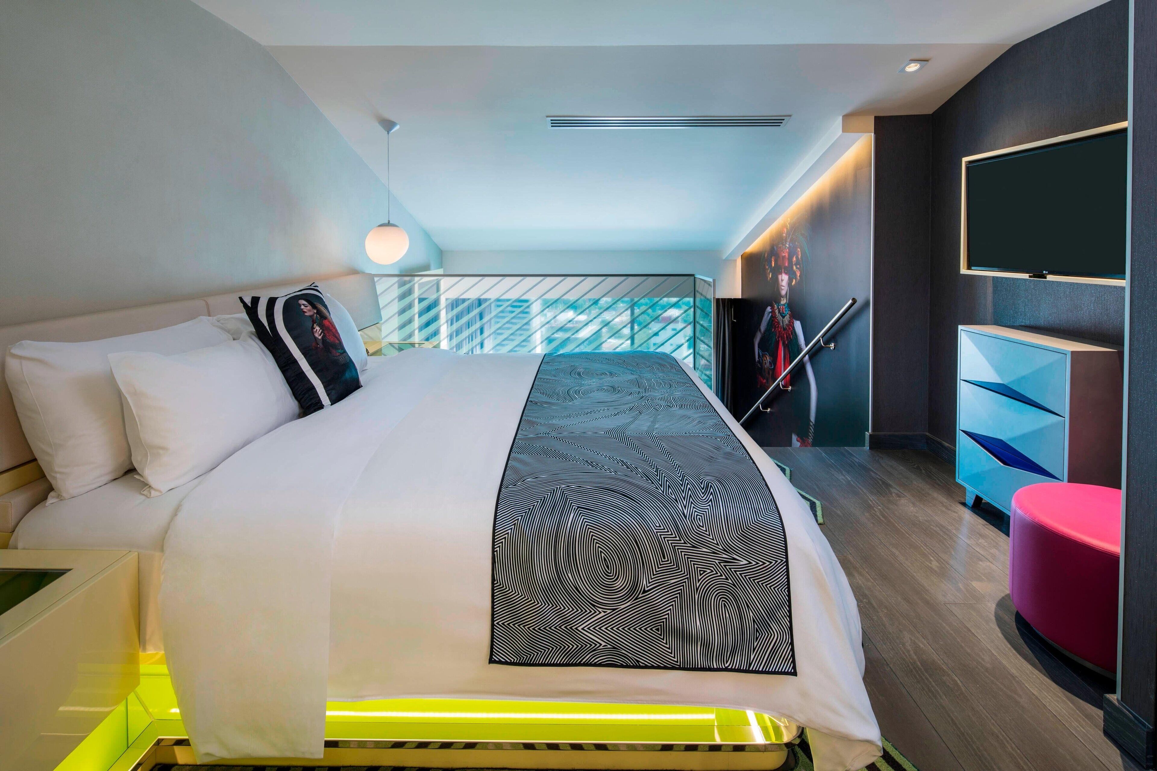 Une chambre d’hôtel moderne dotée d’un grand lit, d’un téléviseur fixé au mur et d’un balcon avec une balustrade.