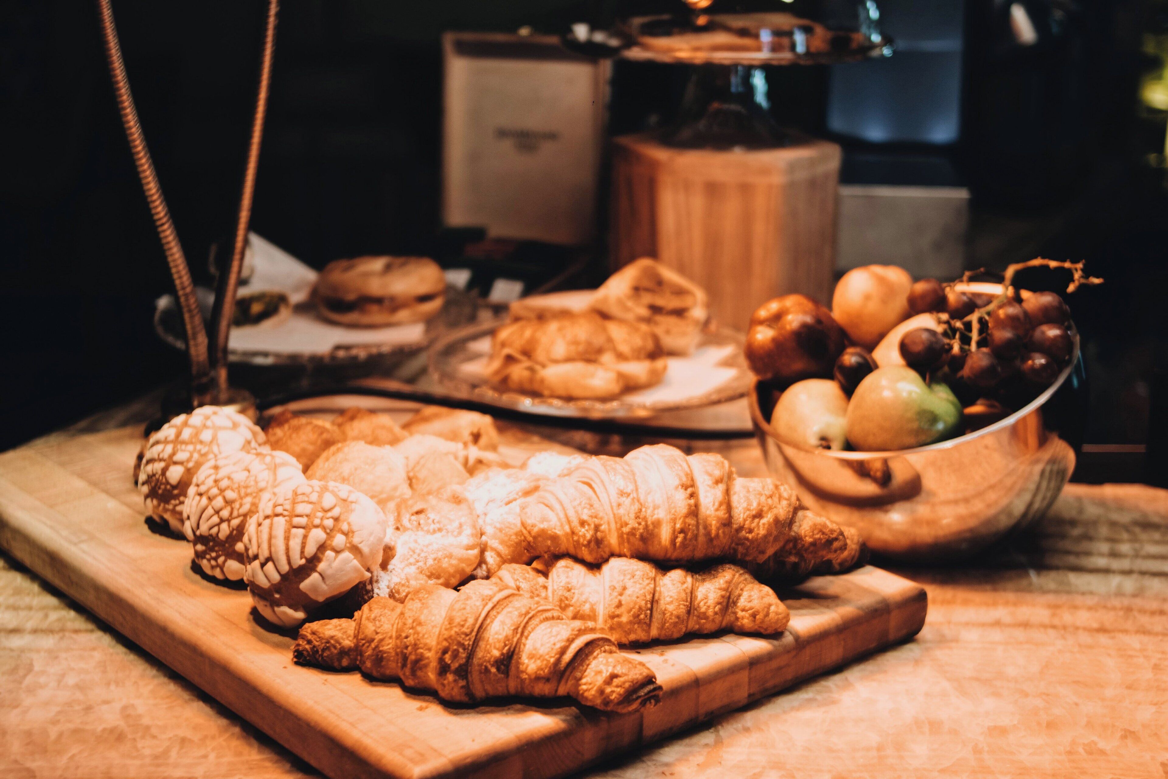 A wooden cutting board with pastries and a bowl of fruit.