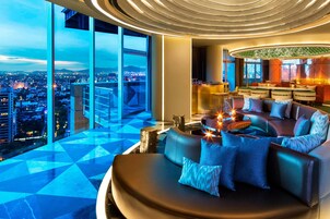 Un salón moderno con vistas panorámicas de la ciudad, un espacio de estar circular y un bar con un diseño único de pared verde.