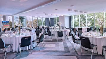 Una amplia sala de conferencias con varias mesas dispuestas para comer, grandes ventanales con vista a la ciudad y una decoración moderna.