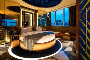 Una habitación de hotel moderna con una cama redonda, un ventanal con vistas a la ciudad, un minibar y un área de descanso con vistas.