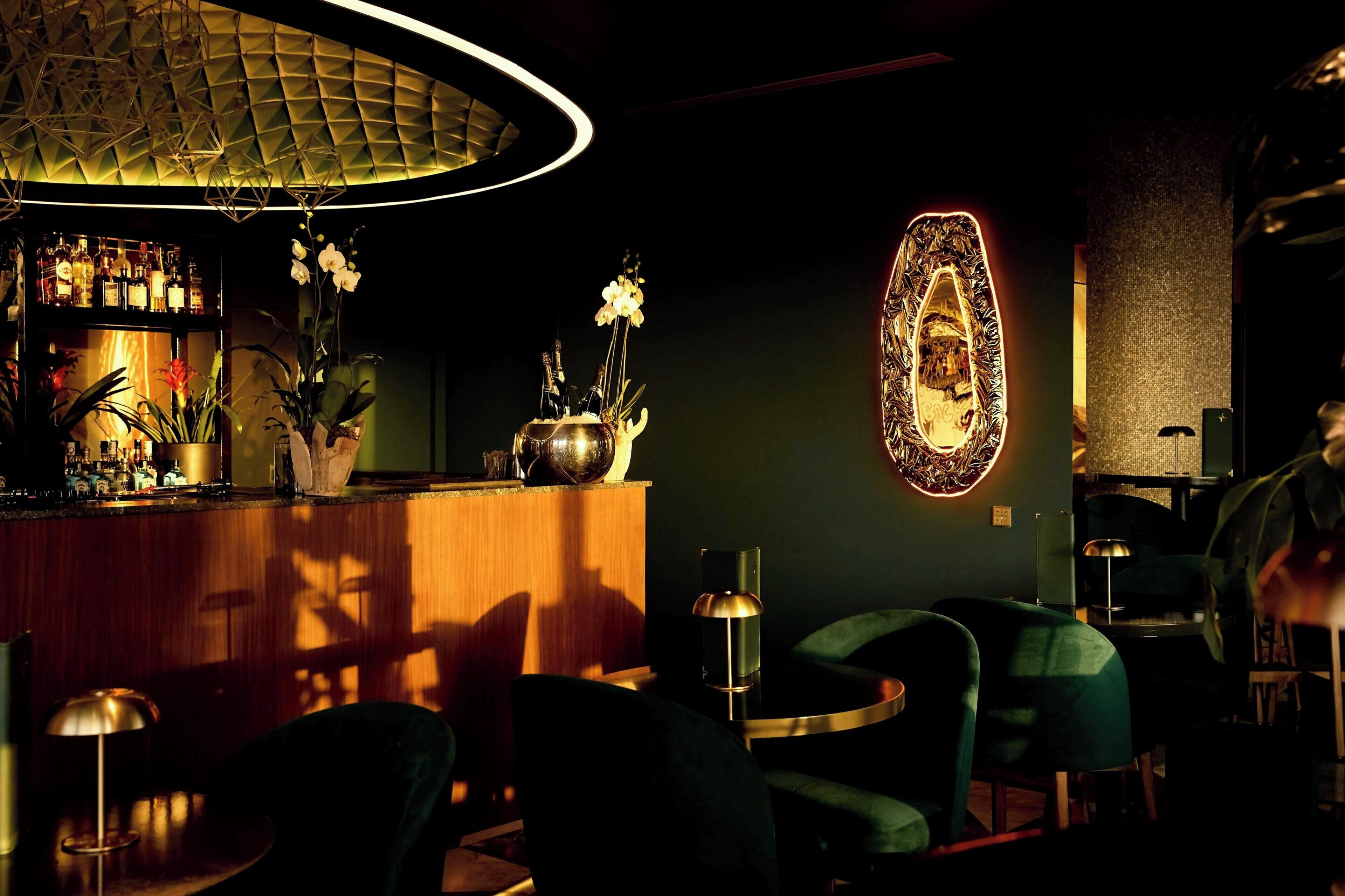 Un área de bar con mostrador de madera, sillas verdes y un espejo decorativo.