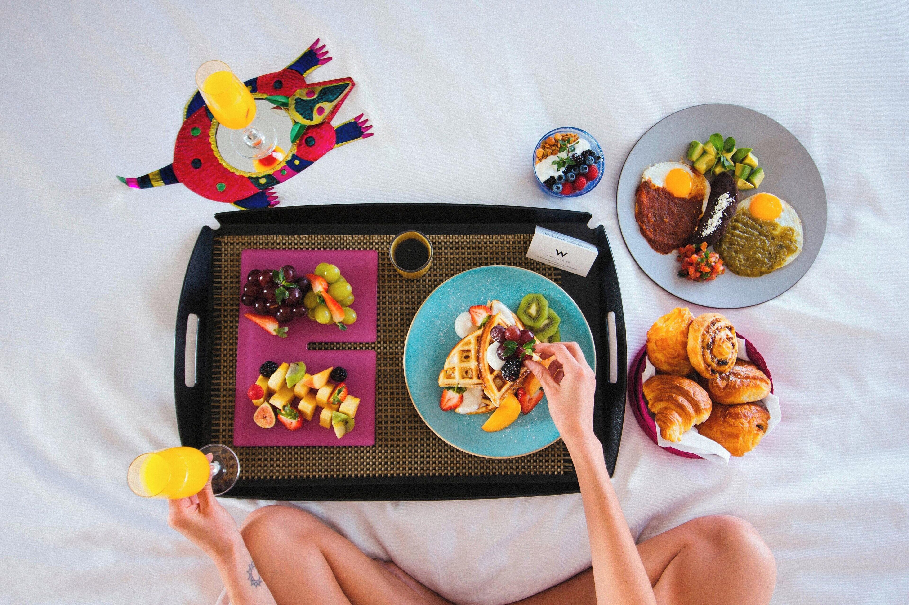 Bandeja de desayuno con waffles, fruta y pastelería sobre la cama.