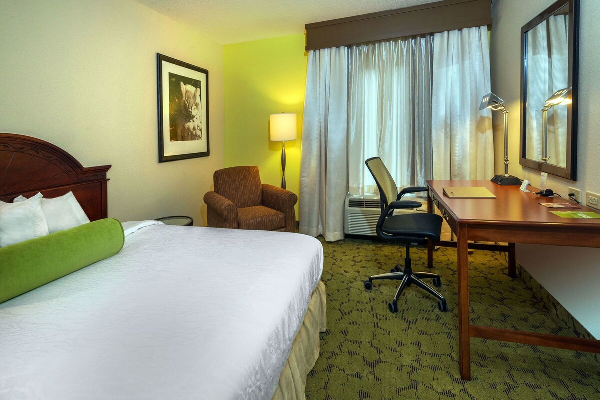 A hotel room with a bed, a desk, a chair, a lamp, and a picture on the wall.