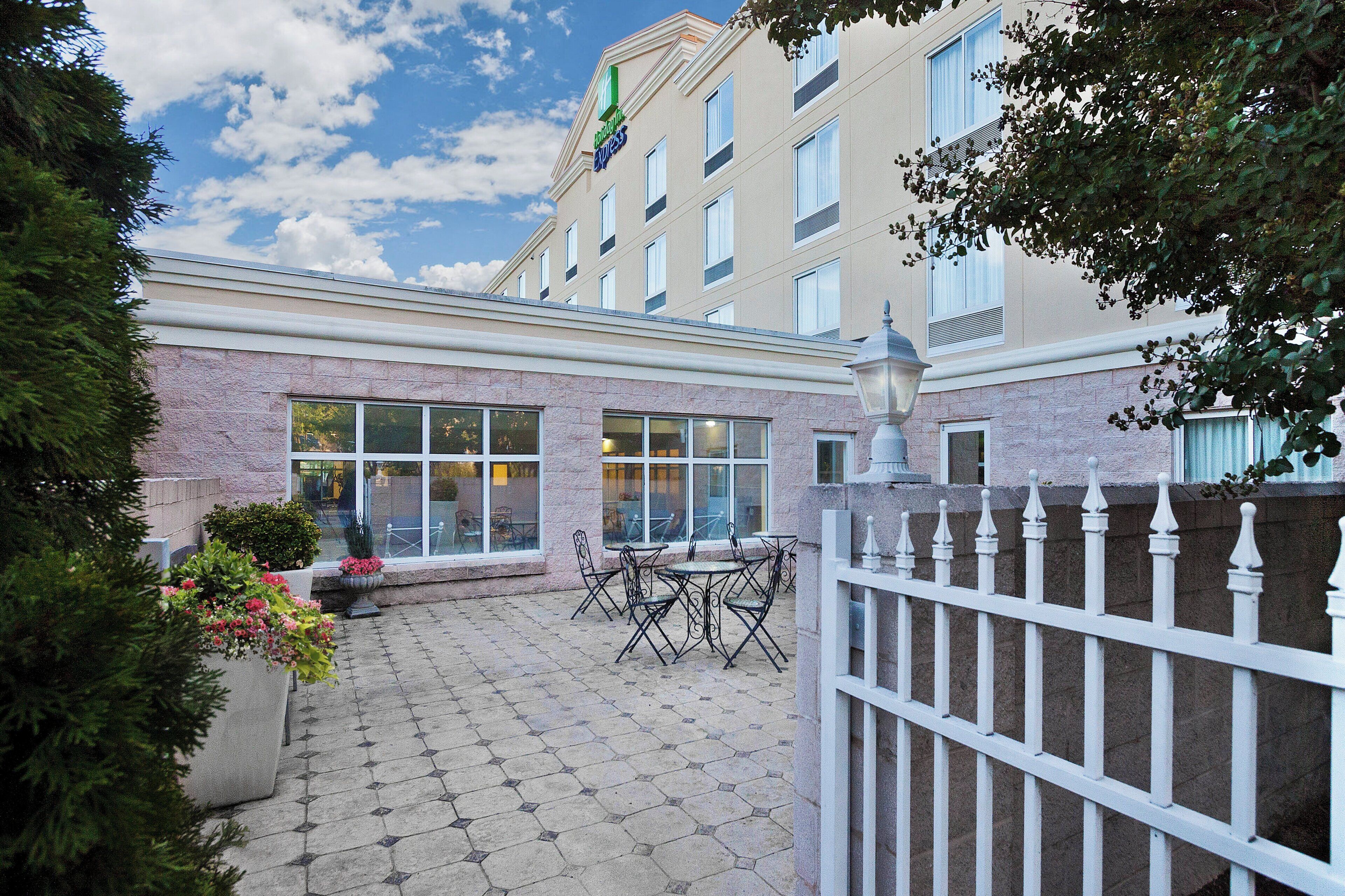 A hotel courtyard with a paved patio, outdoor seating, and a white fence.