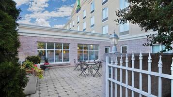 A hotel courtyard with a paved patio, outdoor seating, and a white fence.