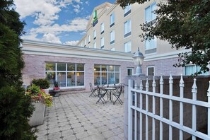A hotel courtyard with a paved patio, outdoor seating, and a white fence. - Holiday Inn Express Hotel & Suites Concord by IHG (Kannapolis)