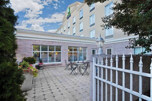 A hotel courtyard with a paved patio, outdoor seating, and a white fence.