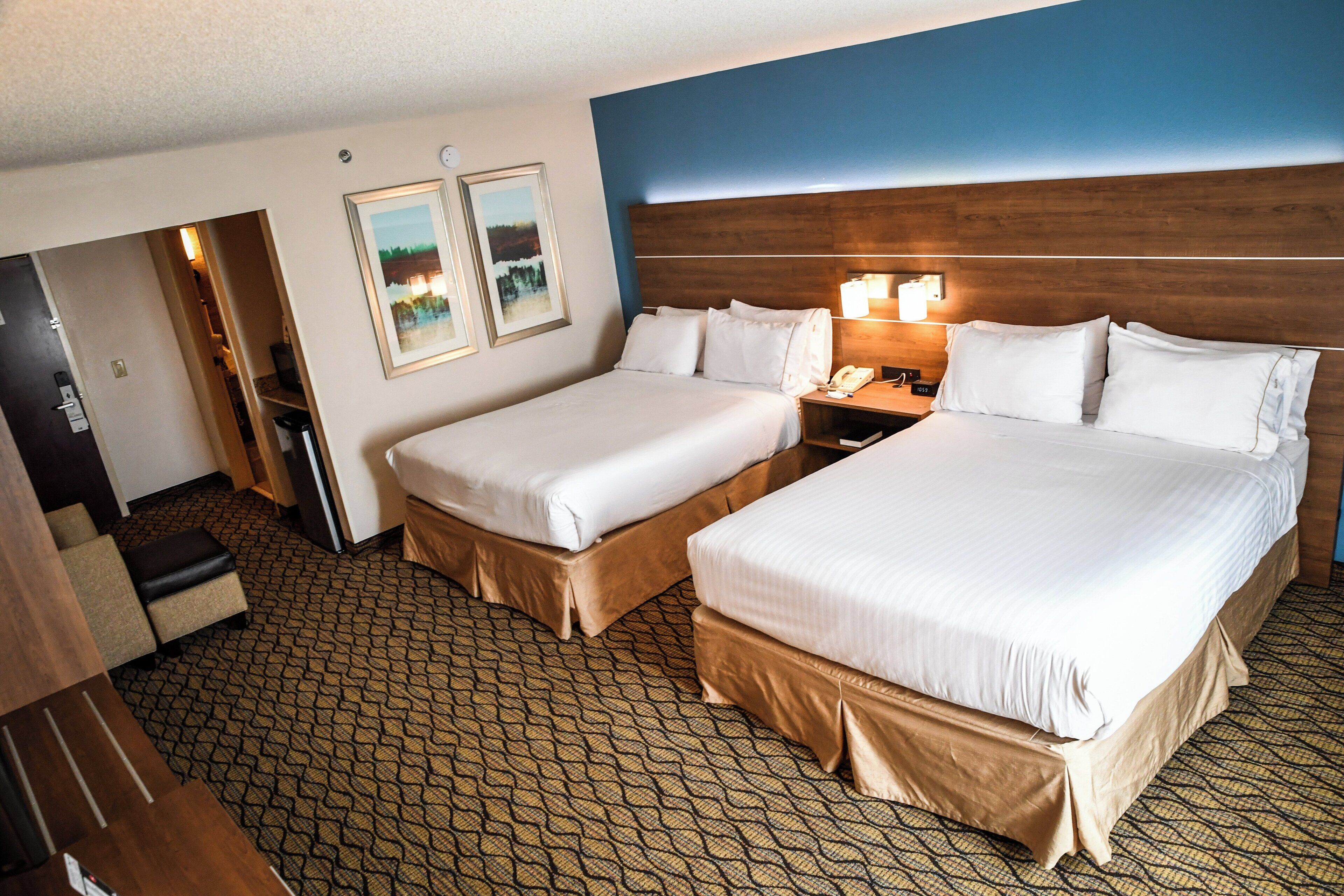 A hotel room with two beds, a wooden headboard, a nightstand with a lamp, and a door leading to a bathroom.