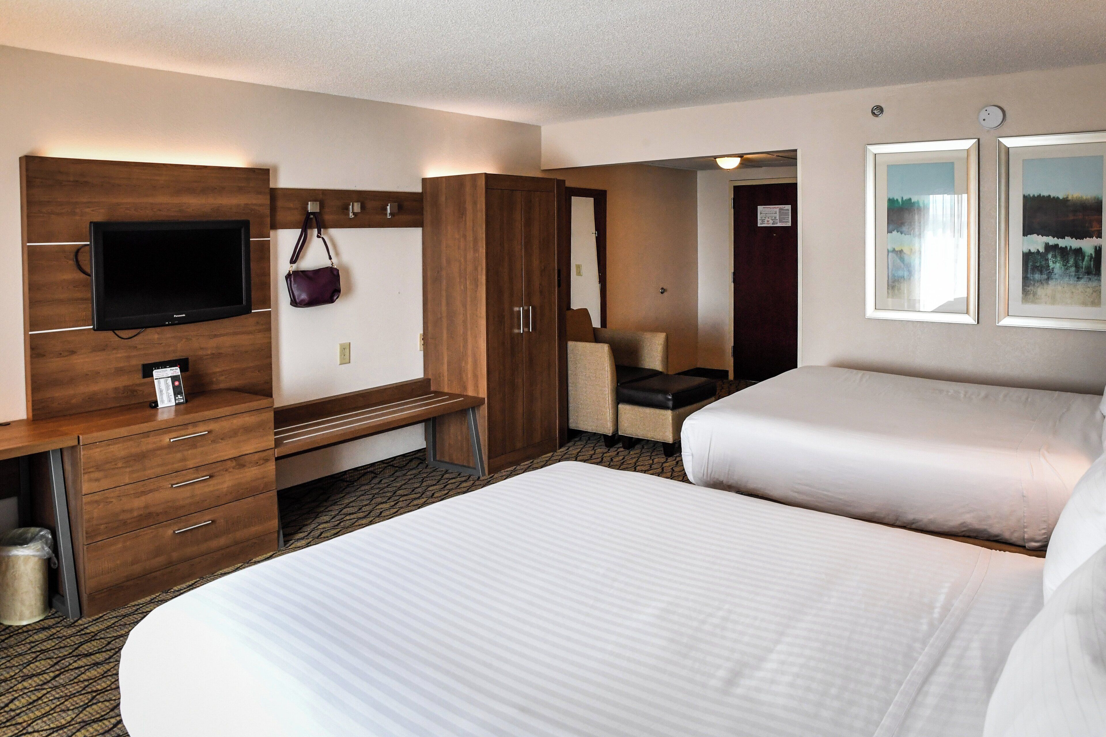 Quarto de hotel com duas camas, uma escrivaninha, televisão e uma cadeira.