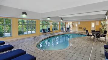Área da piscina com elevador, cadeiras e vista para árvores através de grandes janelas.