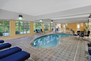A swimming pool area with a pool lift, chairs, and a view of trees through large windows. - Holiday Inn Express Hotel & Suites Concord by IHG (Kannapolis)