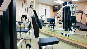 Une salle de sport équipée de divers appareils d’exercice, d’un tapis de course et d’un miroir qui reflète la pièce.