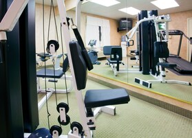 A gym with various exercise equipment, a treadmill, and a mirror reflecting the room.