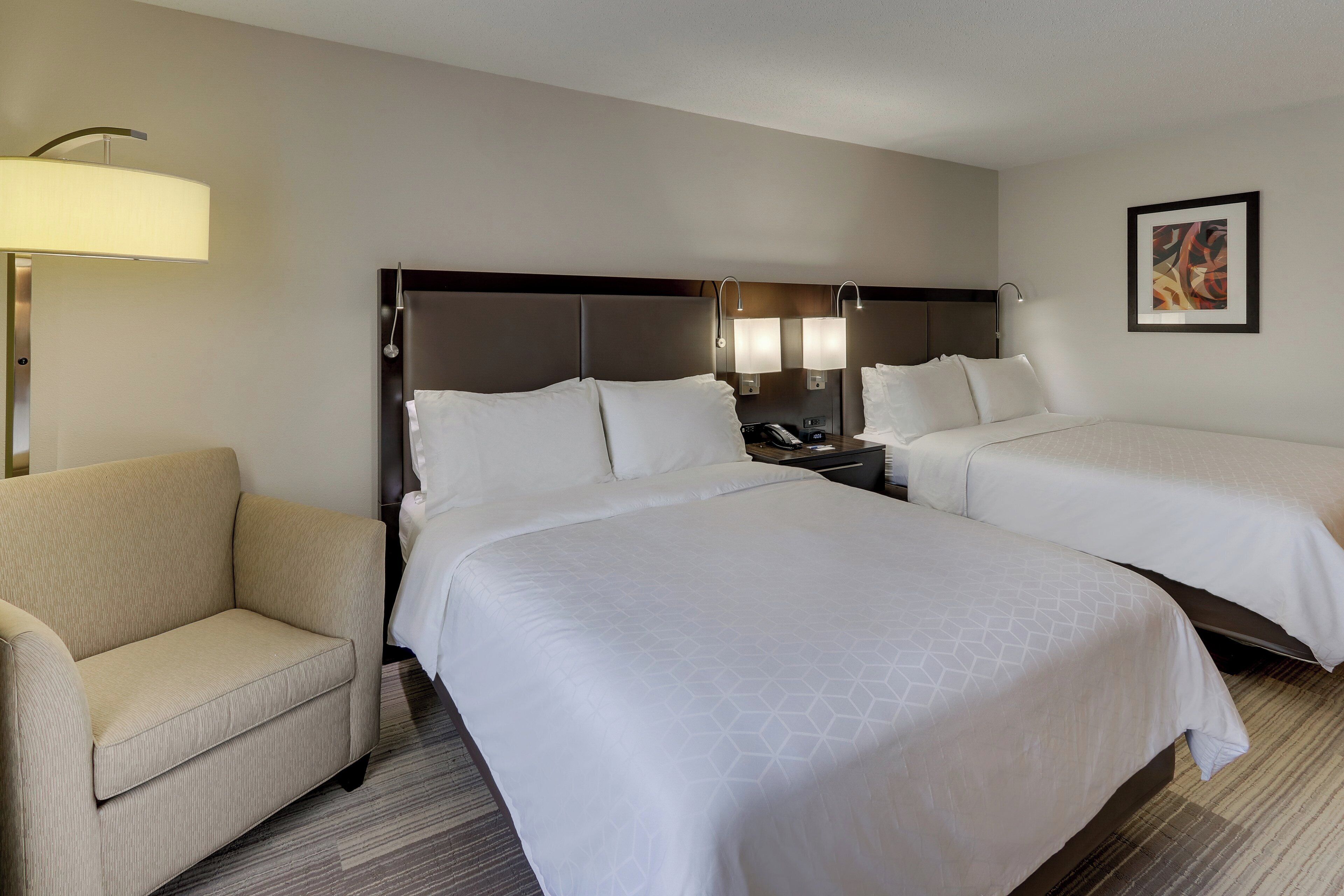 A hotel room with two beds, a sofa, a nightstand, and a lamp.