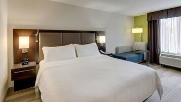 A hotel room with a large bed, bedside tables, a chair, a lamp, and a window with curtains.