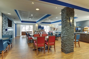 A modern dining area with wooden flooring, red and blue seating, and a stone accent wall. - Holiday Inn Express Hotel & Suites Dayton-Centerville by IHG (Dayton)