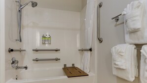 A bathroom with a bathtub, grab bars, a towel rack, and a shelf with toiletries. - Holiday Inn Express Hotel & Suites Dayton-Centerville by IHG (Dayton)