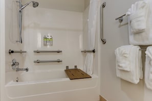 A bathroom with a bathtub, grab bars, a towel rack, and a shelf with toiletries.