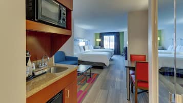 Habitación de hotel con kitchenette, cama, escritorio y silla.