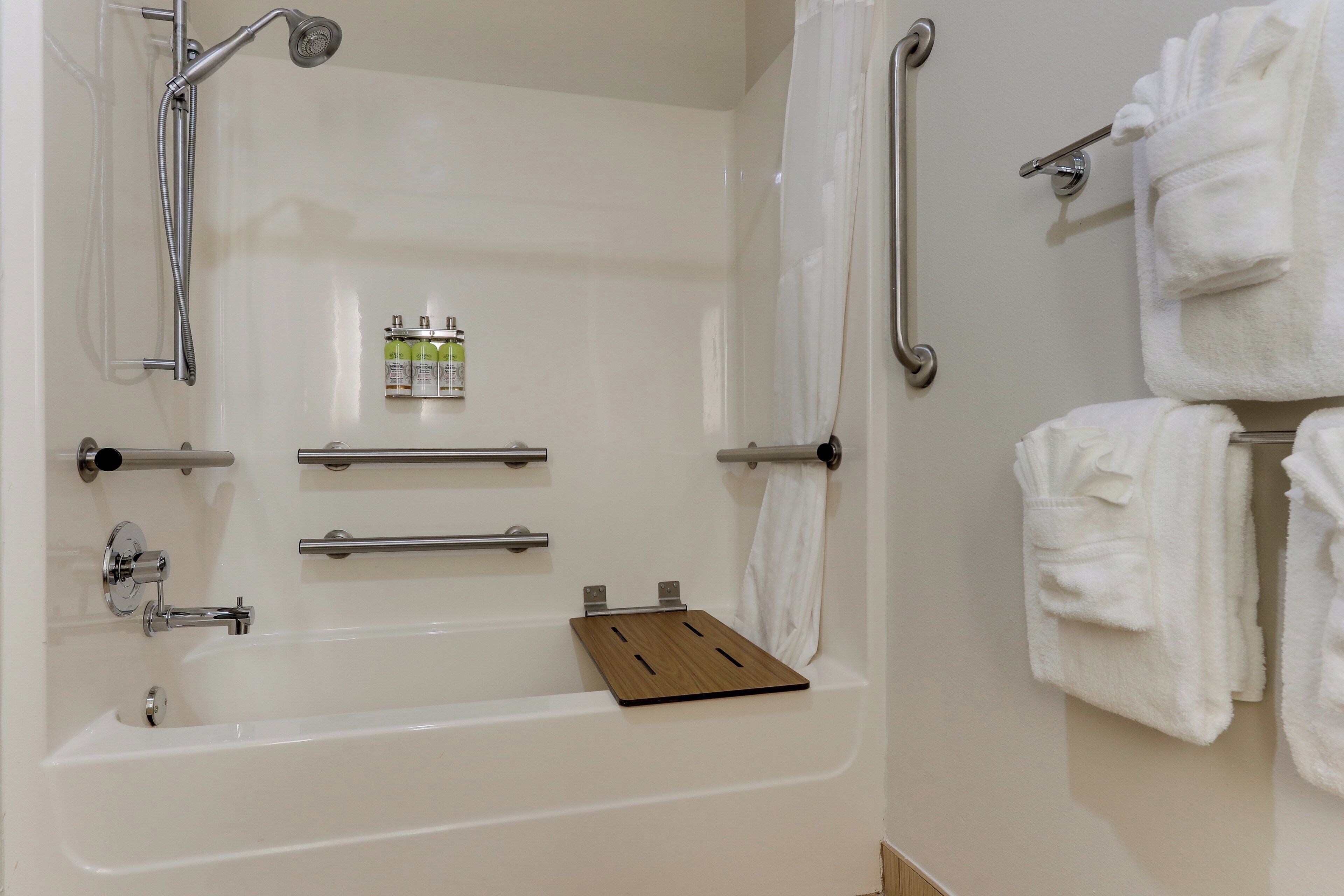 Ein Badezimmer mit Badewanne, Haltegriffen, einem Handtuchhalter und einem Ablagefach mit Toilettenartikeln.