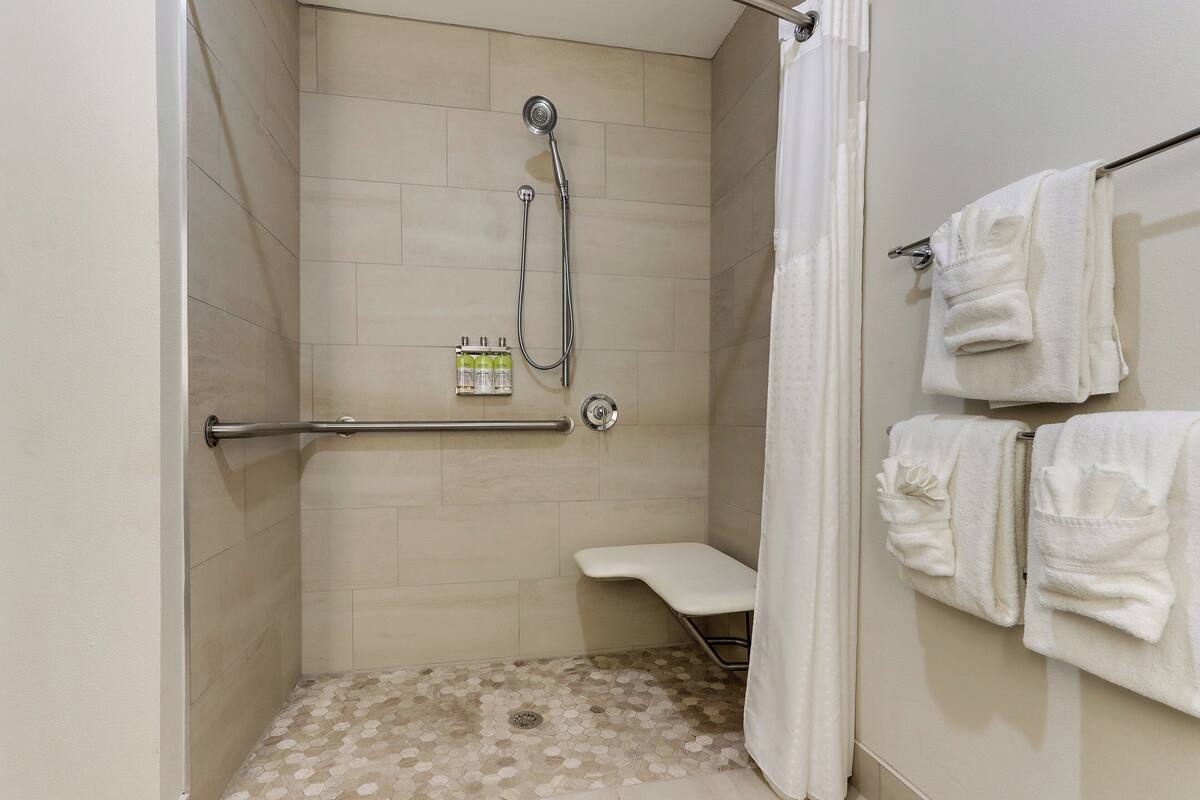 A shower with a handheld showerhead, a grab bar, and a white towel rack with towels.