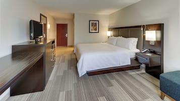 A hotel room with a bed, bedside table, lamp, TV, and a desk.