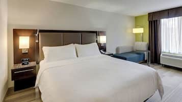 A hotel room with a large bed, bedside tables, a chair, a lamp, and a window with curtains.