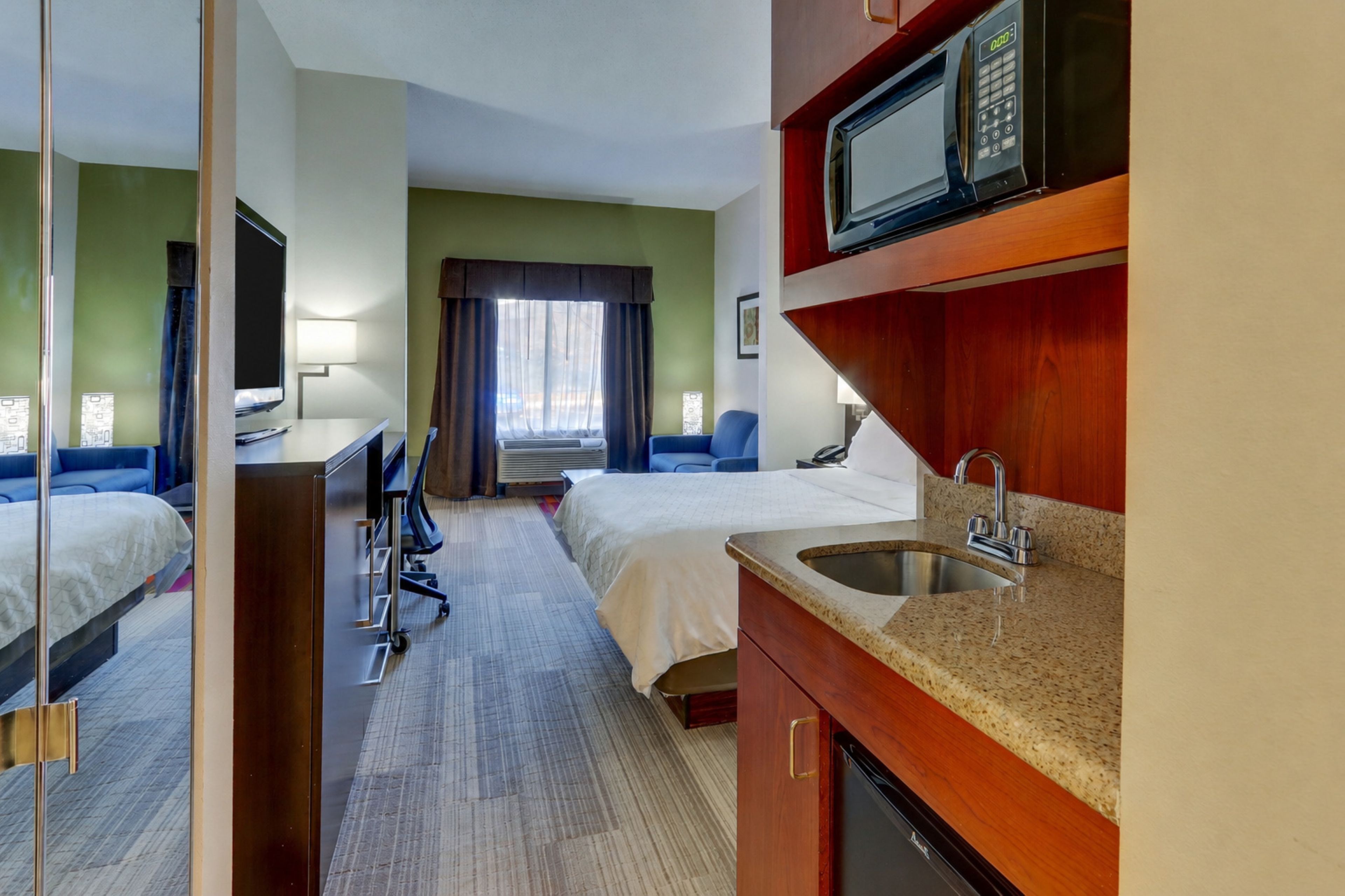 A hotel room with two beds, a desk, a microwave, and a sink.