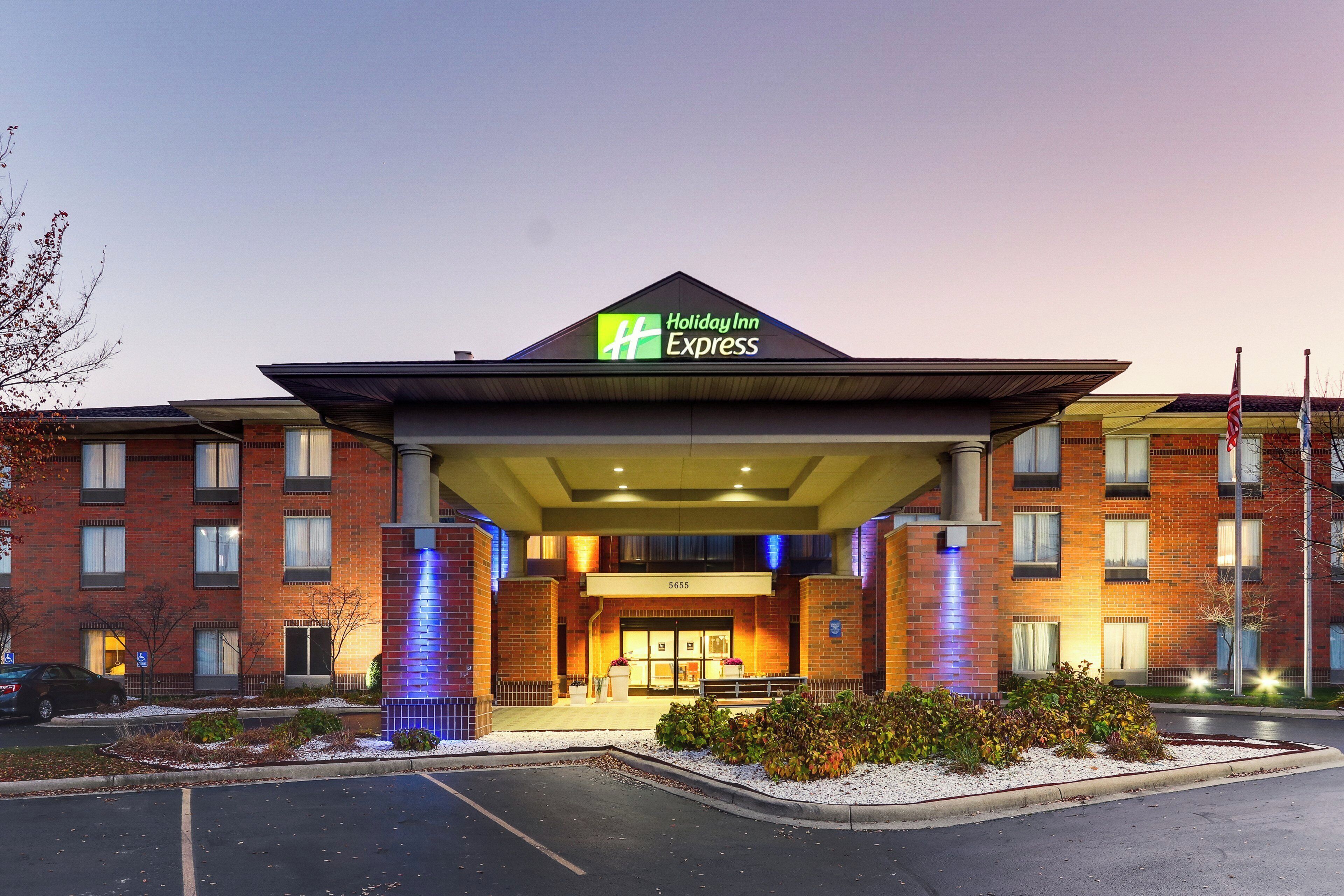 Un hotel Holiday Inn Express con fachada de ladrillo, un acceso cubierto y un estacionamiento.