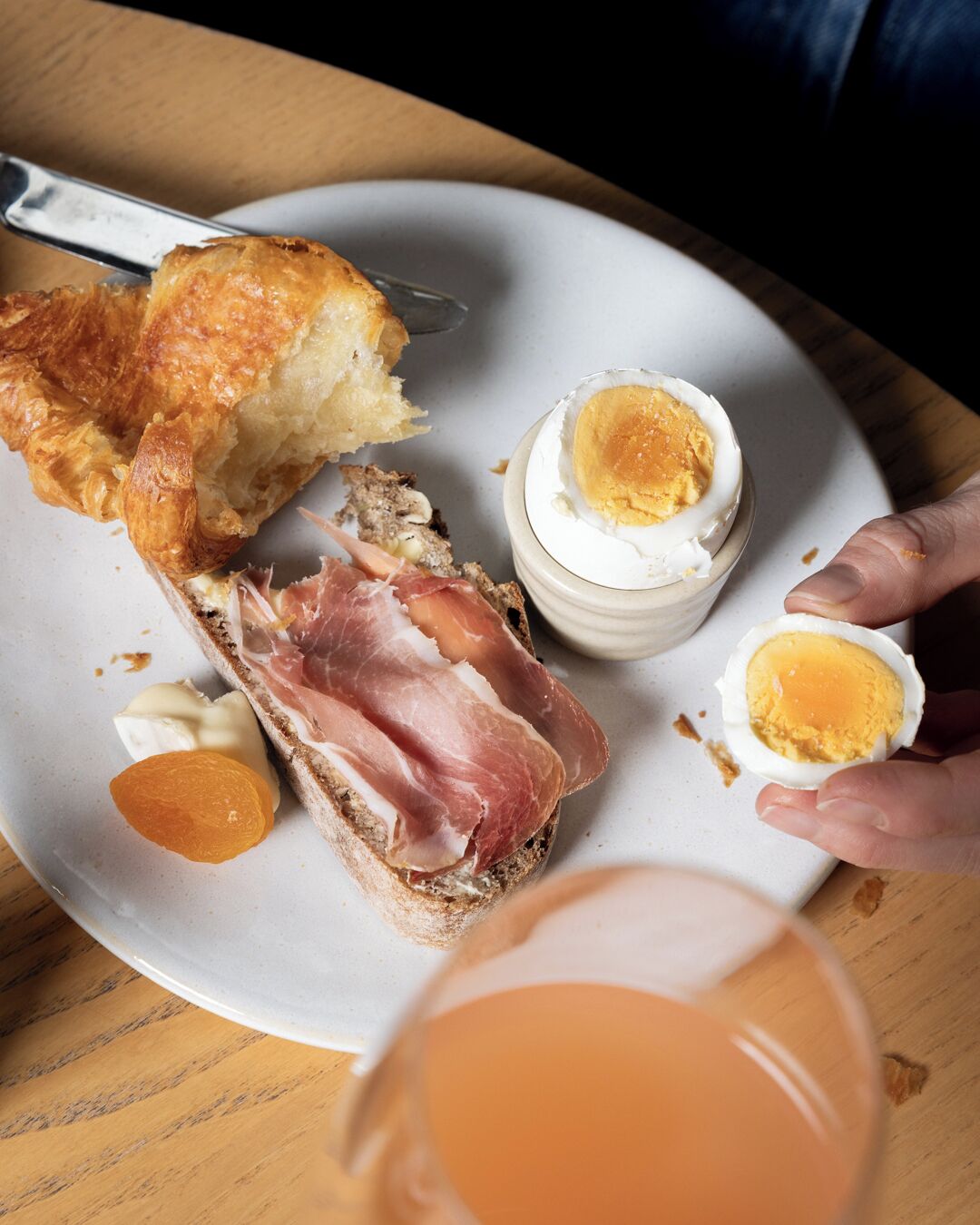 Une assiette avec un croissant, une tranche de pain garnie de jambon et de fromage, un œuf dur et une petite tranche d’orange.