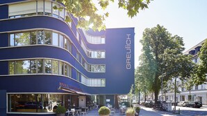 A multi-story hotel with a curved facade, large windows, and outdoor seating area. - Greulich Design & Boutique Hotel (Zürich)