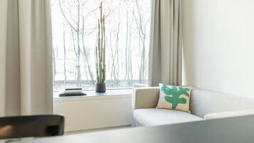 Ein modernes Wohnzimmer mit einer Couch, einem kleinen Tisch und einem Fenster mit Blick auf Bäume.