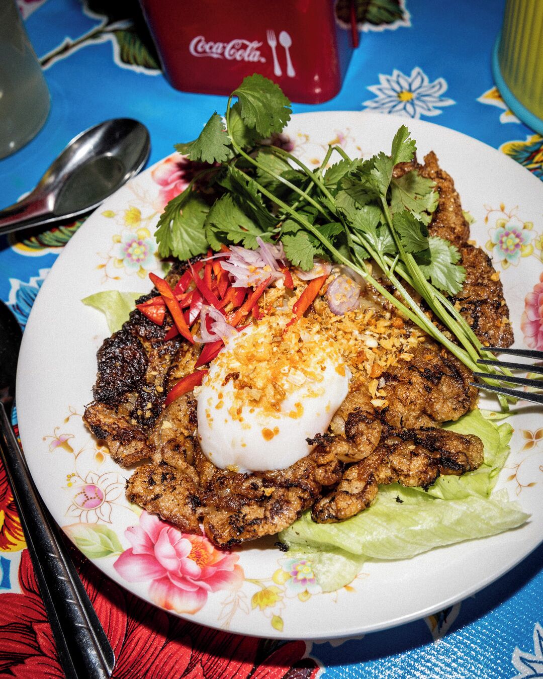 A plate of grilled meat with vegetables and a poached egg on a floral tablecloth.
